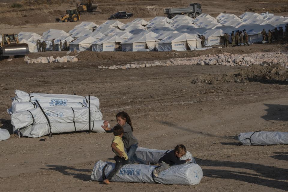 Children play as Greek soldiers install tents at a temporary camp near Mytilene town, on the northeastern island of Lesbos, Greece, Saturday, Sept. 12, 2020. Greek authorities have been scrambling to find a way to house more than 12,000 people left in need of emergency shelter on the island after the fires deliberately set on Tuesday and Wednesday night gutted the Moria refugee camp. (AP Photo/Petros Giannakouris)
