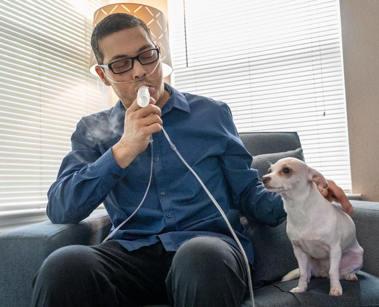 Charles Richard uses his nebulizer sitting beside his dog Chulita. Charles has been diagnosed with stage IV lung cancer and is in treatment, but he hopes to one day return to working. His wife has become his full-time caregiver.