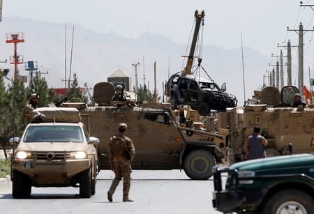 Afghan security forces stand guard at the site of a suicide attack while others remove a wreckage of a car damaged in the attack, in Kabul