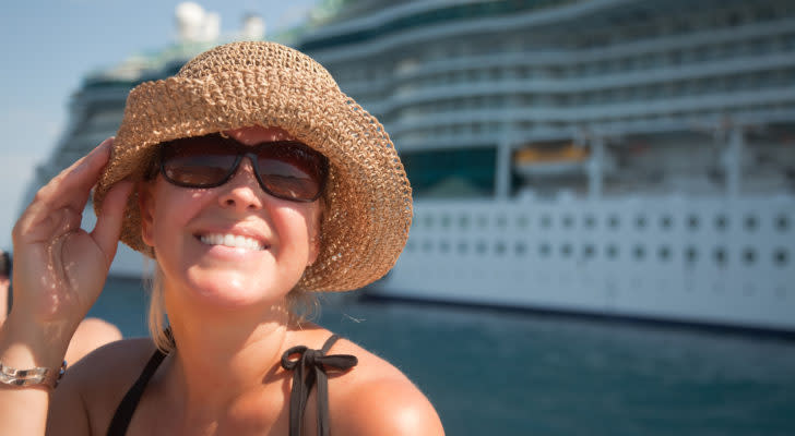 A close-up shot of a woman wearing a straw hat with a cruise ship in the background. Cruise stocks are in the news again today.