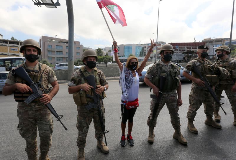 Demonstrator raises Lebanese flag while standing between soldiers in Baabda