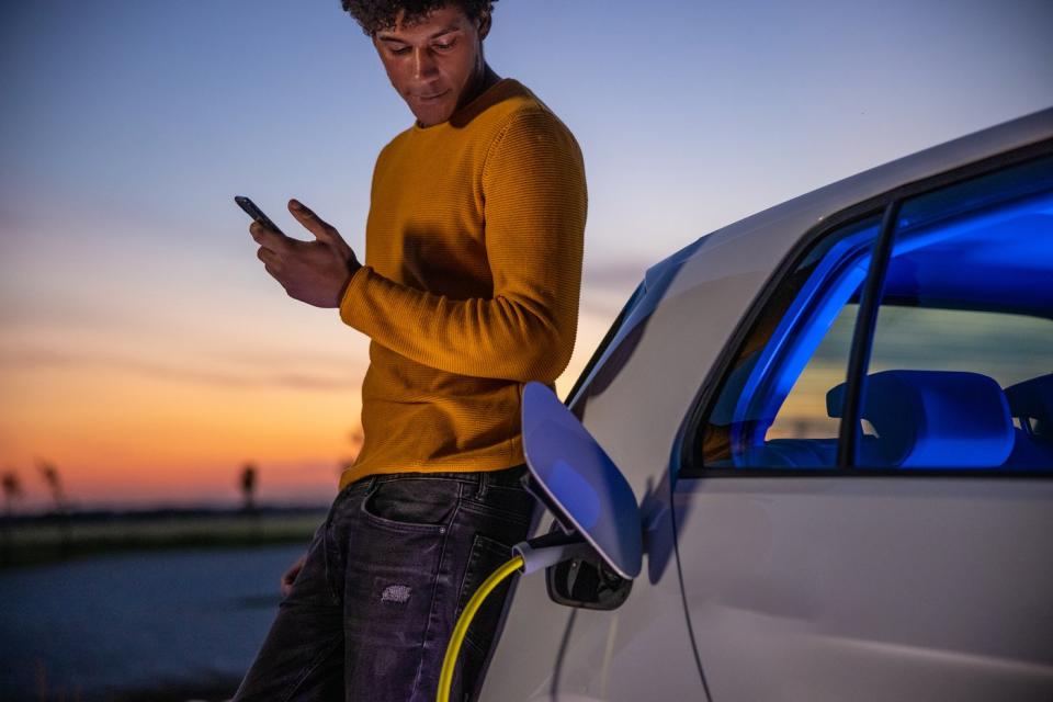 A person uses a smartphone while charging an EV.