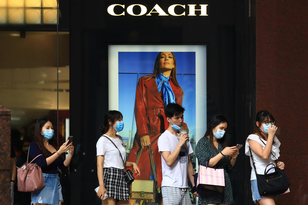 SINGAPORE - JUNE 20:  Shoppers wearing protective masks walk past a COACH boutique at Orchard Road on June 20, 2020 in Singapore. From June 19, Singapore started to further ease the coronavirus (COVID-19) restrictions by allowing social gatherings up to five people, re-opening of retail outlets and dining in at food and beverage outlets, subjected to safe distancing. Parks, beaches, sports amenities and public facilities in the housing estates will also reopen. However, large scale events, religious congregations, libraries, galleries and theatres will remain closed.  (Photo by Suhaimi Abdullah/Getty Images)