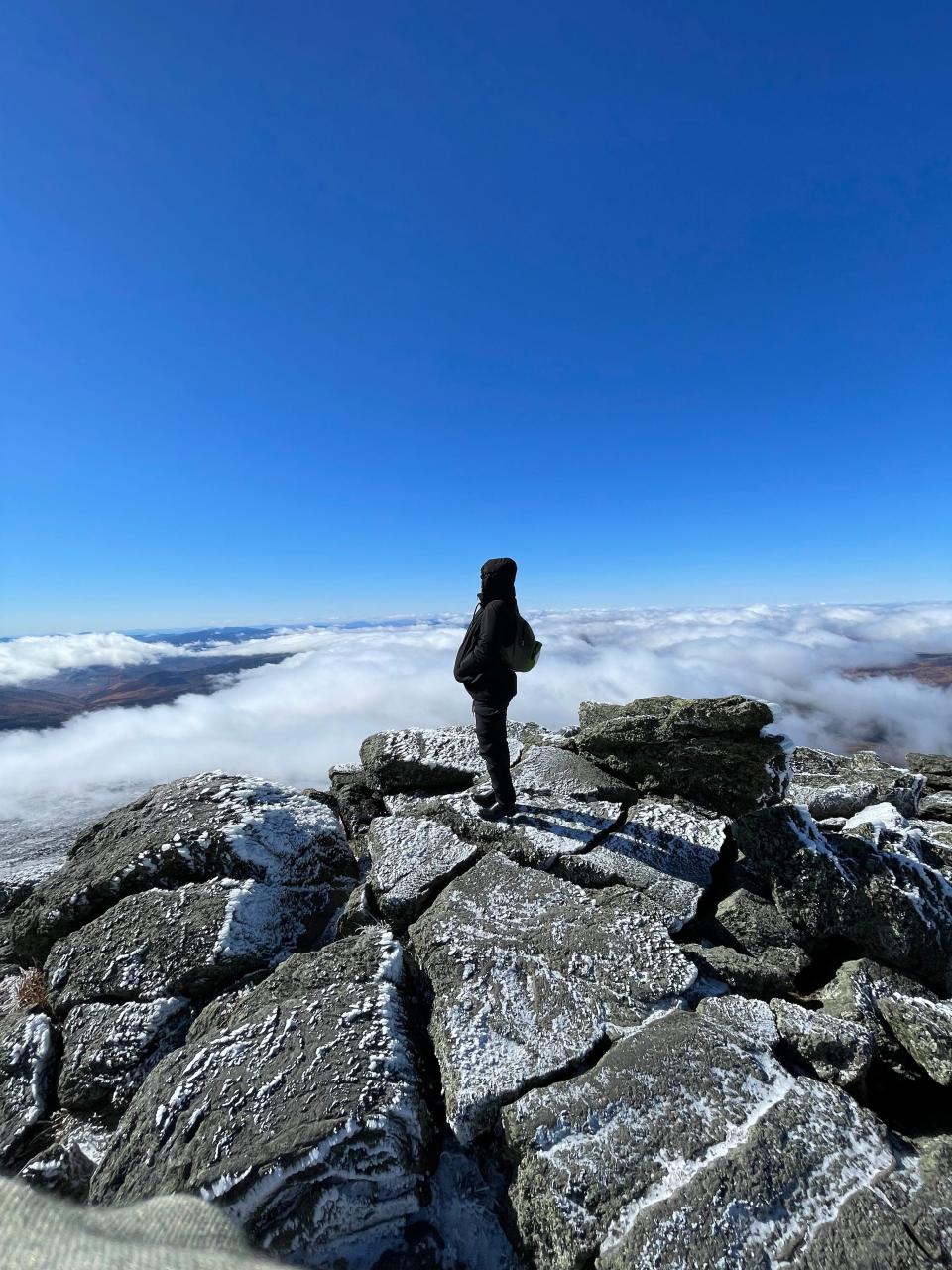 A figure standing on the edge of a mountain backdropped by clouds