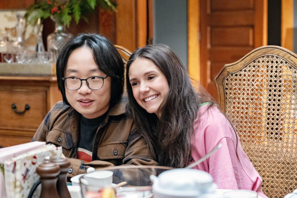 Jimmy O. Yang and Nina Dobrev smiling and sitting close together at a dining table in a cozy indoor setting