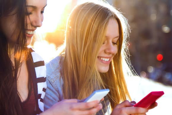 Two smiling young women using their smartphones to surf the internet and text.