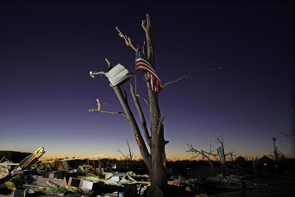 An American flag hangs from a damaged tree Sunday, Dec. 12, 2021, in Mayfield, Ky. Tornadoes and severe weather caused catastrophic damage across several states Friday, killing multiple people. (AP Photo/Mark Humphrey)