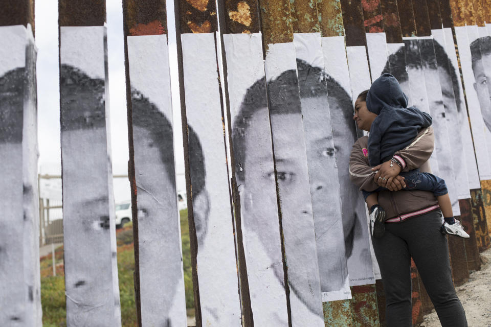 <p>A member of the Central American migrant caravan, holding a child, looks through the border wall toward a group of people gathered on the U.S. side, near the beach where the border wall ends in the ocean, in Tijuana, Mexico, April 29, 2018. (Photo: Hans-Maximo Musielik/AP) </p>