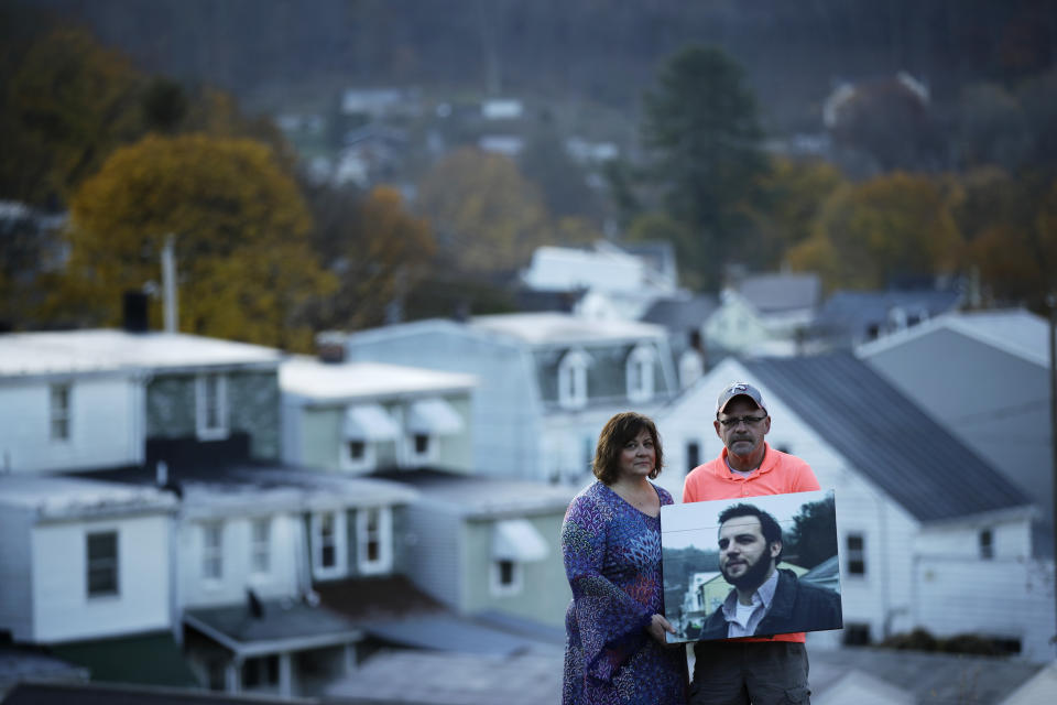 In this Nov. 8, 2018 photo, Janel Wentz and Tim Firestone pose for a photograph in Port Carbon, Pa. while holding an image of their late son former Mount Carbon Mayor Brandon Wentz. Wentz's family is speaking out for the first time about his sudden death one year ago. Wentz was 22 when he became mayor of Mount Carbon, population 87. He died suddenly last November at age 24, just hours after resigning from office due to a family move. Wentz's family says he died of an overdose of heroin and fentanyl. His passing came near the end of a year that saw a record number of drug overdose deaths. (AP Photo/Matt Rourke)