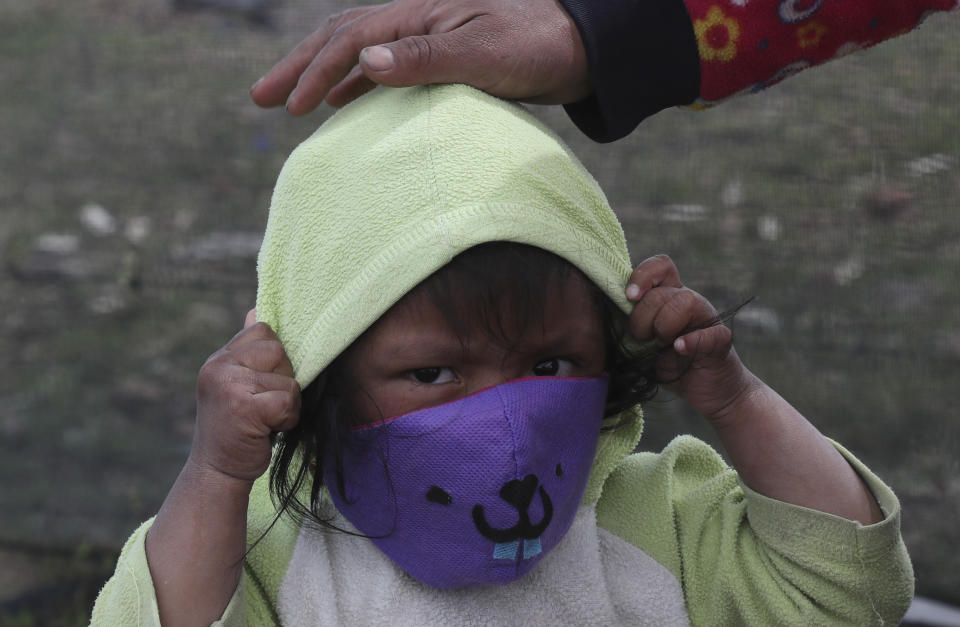 An Indigenous child puts on a mask to curb the spread of the new coronavirus while walking with his mother through the fields in Cayambe, Ecuador, Wednesday, June 17, 2020. Indigenous communities in Ecuador have implemented their security methods to prevent the virus from entering their lands, especially since they do not have health centers that can take care of them if the disease becomes serious. (AP Photo/Dolores Ochoa)