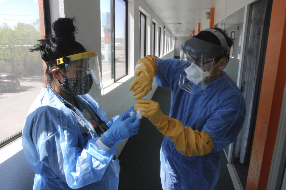 FILE - In this May 7, 2020, file photo, Certified Medical Assistant Shaniya Wood, left, and physician Caleb Lauber, right, test one of over 100 homeless patients who were being isolated in motels for the coronavirus in Gallup, N.M. Some 140 people are participating in the impromptu system, and officials hope it will interrupt a treadmill of infections among Gallup’s homeless population. (AP Photo/Morgan Lee, File)