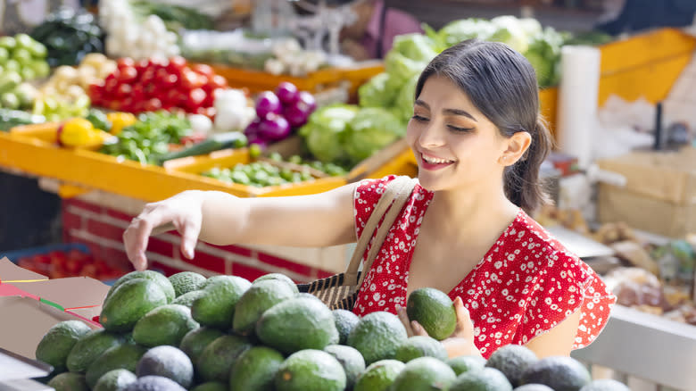 A smiling woman picking avocados at a market