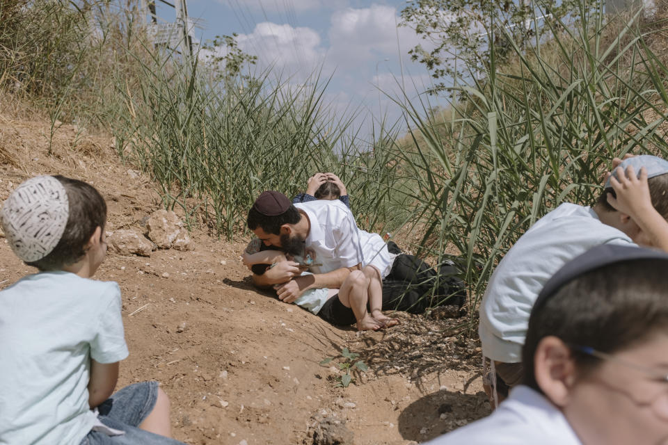 Israelis take cover as a siren sounds a warning of incoming rockets fired from the Gaza Strip in Rehovot, Israel, Friday, Oct. 13, 2023. (AP Photo/Dor Kedmi)