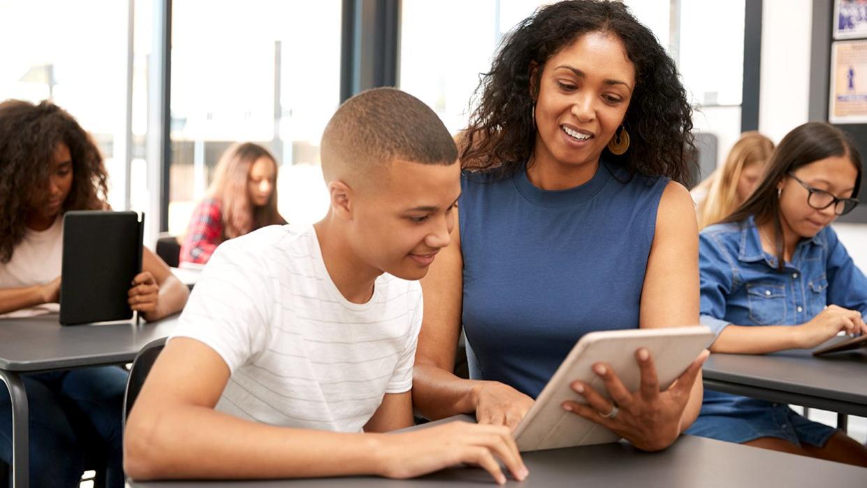 public school teacher helping student classroom desk