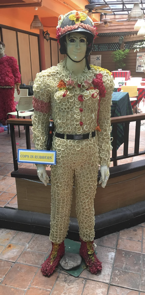 A cop mannequin with a head-to-toe condom outfit, including shoes and a helmet embellished with condoms, with a "Cops in Rubbers" sign