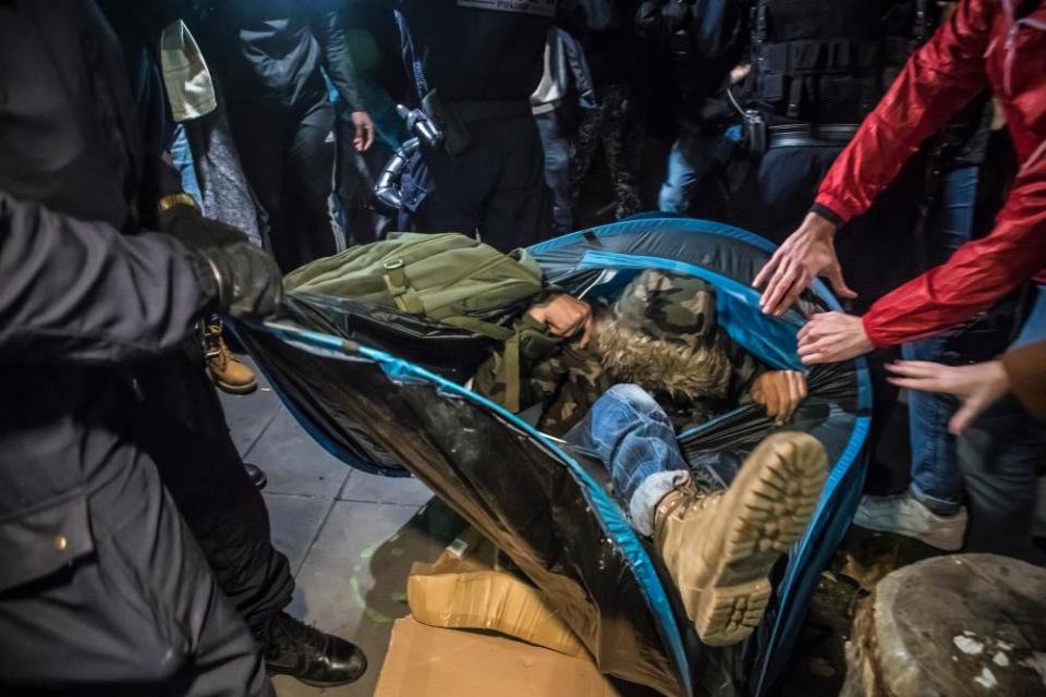 A protester encased in a collapsed tent is removed