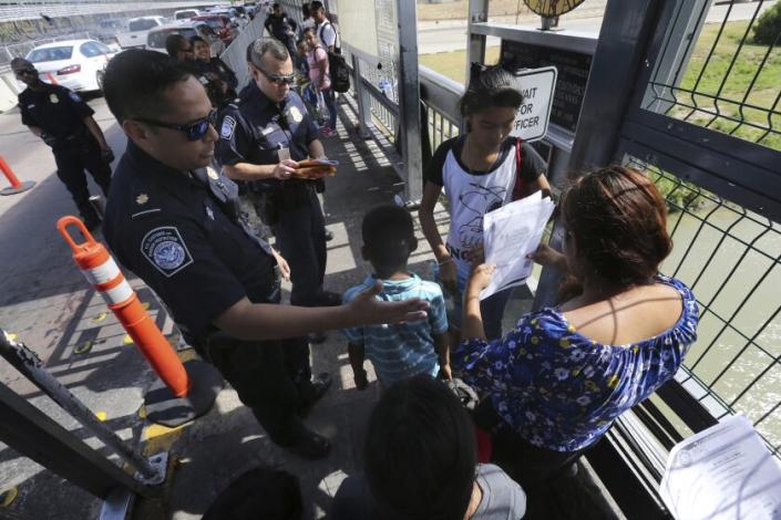 FILE - In this July 17, 2019 file photo, a U.S. Customs and Border Protection officer checks the documents of migrants before they are taken to apply for asylum in the United States at International Bridge 1 in Nuevo Laredo, Mexico.  On Wednesday, July 24, 2019, a federal judge in San Francisco will hear arguments in a challenge to the new Trump administration policy that requires asylum seekers crossing a third country en route to the United States to first apply for protection in the other country.  The lawsuit was filed by the American Civil Liberties Union, the Southern Poverty Law Center and the Center for Constitutional Rights as they seek a temporary restraining order to block the plan.  (AP Photo/Marco Ugarte, File