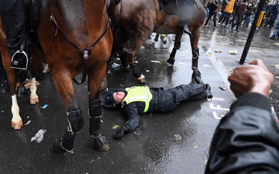 A mounted police officer lays on the road after being unseated from their horse, during a demonstration on Whitehall, - AFP 