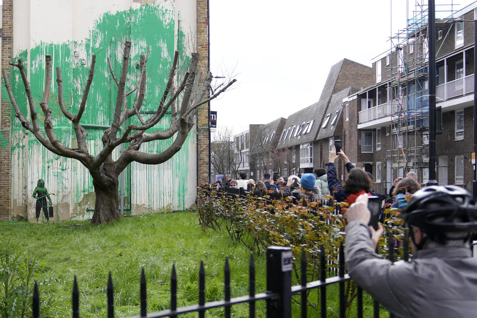 Personas miran un nuevo mural de Banksy en una pared en Londres, el lunes 18 de marzo de 2024. Un nuevo mural de Banksy en el vecindario de Finsbury Park atrajo multitudes a una calle de Londres el lunes, incluso antes de que el esquivo artista de graffiti confirmara que la obra era suya. (Foto AP/Alastair Grant)