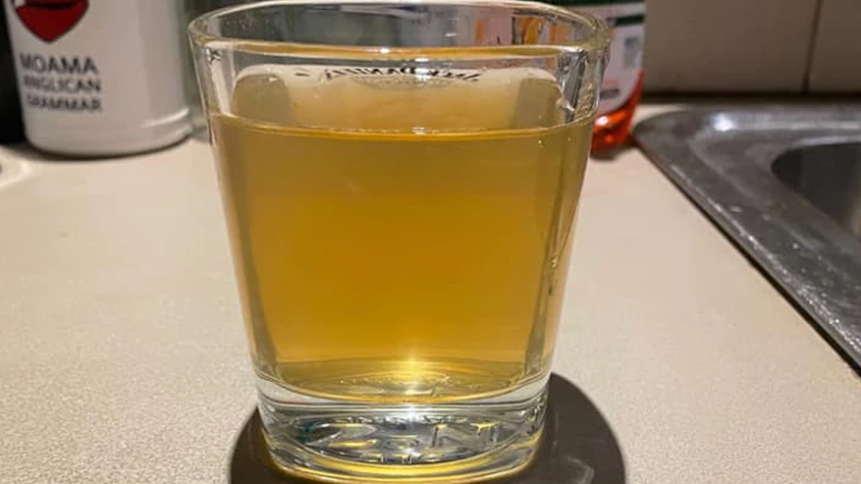 A glass of water containing brown, discoloured water on a kitchen top.