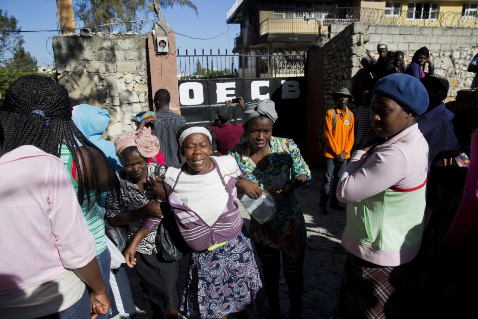 A grieving staff worker of the Orphanage of the Church of Bible Understanding is helped by residents outside the children's home, the morning after a deadly fire broke out in Kenscoff, on the outskirts of Port-au-Prince, Haiti, Friday, Feb. 14, 2020. A fire swept through this orphanage run by a Pennsylvania-based nonprofit group, killing 13 children, according to health care workers. (AP Photo/Dieu Nalio Chery)