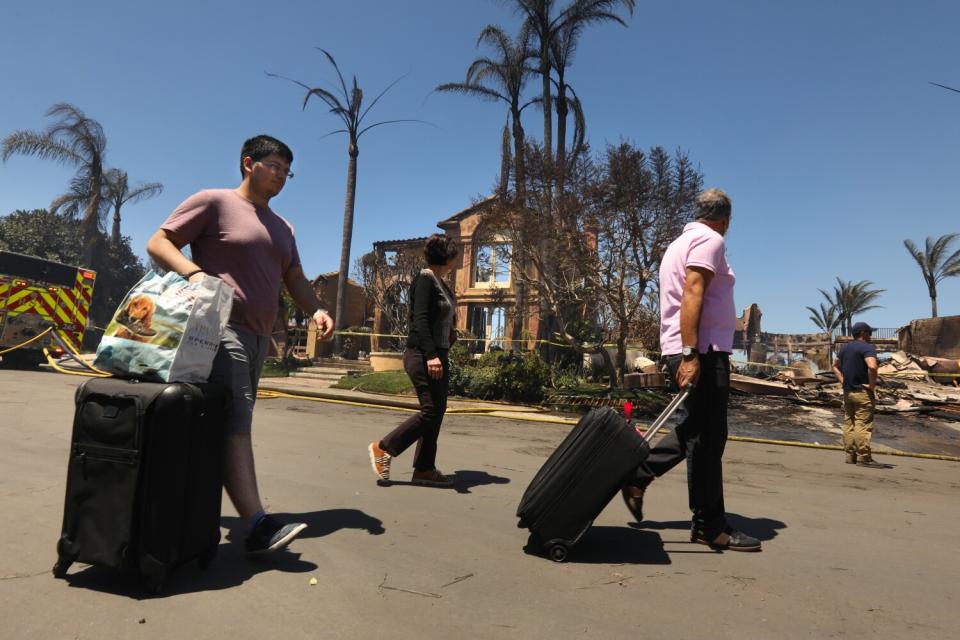 A family leaves with their suitcases after the Coastal fire destroyed more than 20 homes in Laguna Niguel.