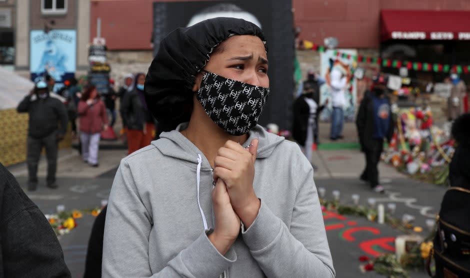 A woman clasping her hands has tears in her eyes in George Floyd Square