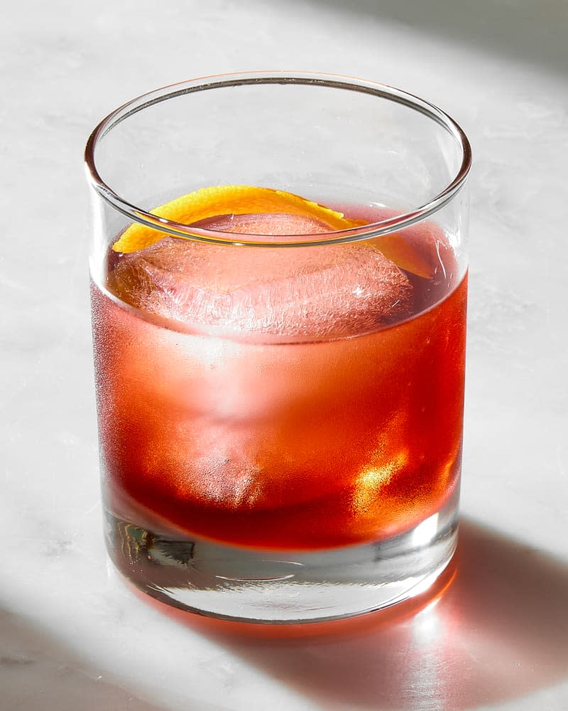 single negroni in a rocks glass, garnished with an orange peel inside of the glass.