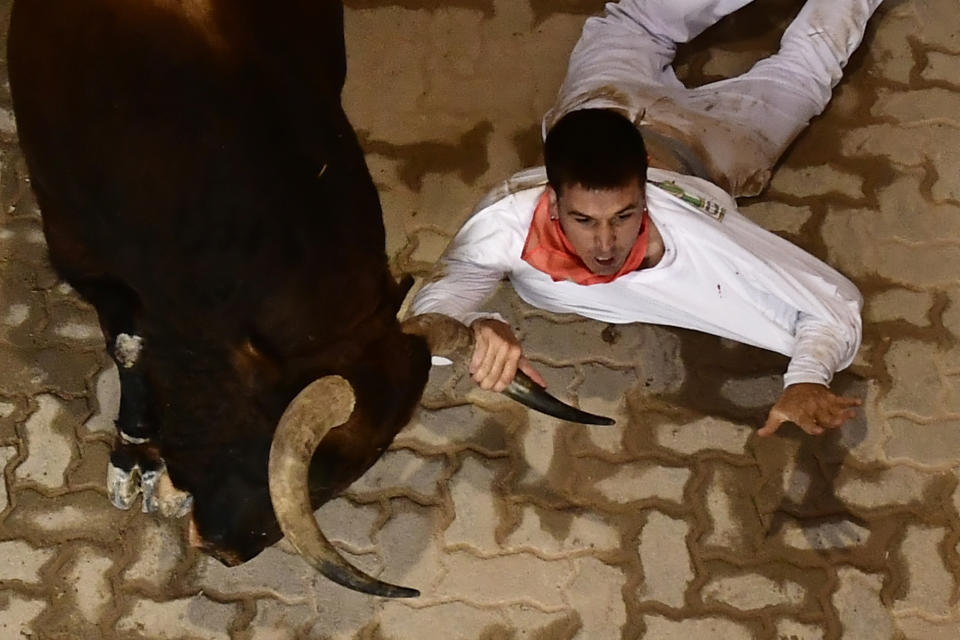 A runner grabs hold of a bull's horns as he falls during the running of the bulls at the San Fermin Festival in Pamplona, northern Spain, Tuesday, July 12, 2022. Revellers from around the world flock to Pamplona every year for nine days of uninterrupted partying in Pamplona's famed running of the bulls festival which was suspended for the past two years because of the coronavirus pandemic. (AP Photo/Alvaro Barrientos)