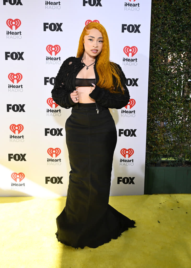 Person stands on event backdrop in black outfit with textured top and long skirt