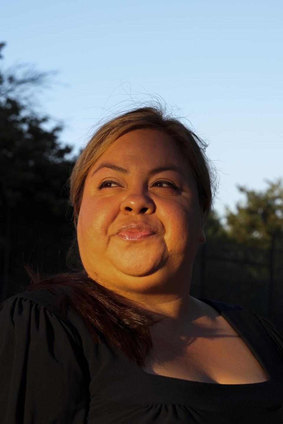 A closeup of a woman with the sun on her face and trees and blue sky behind her