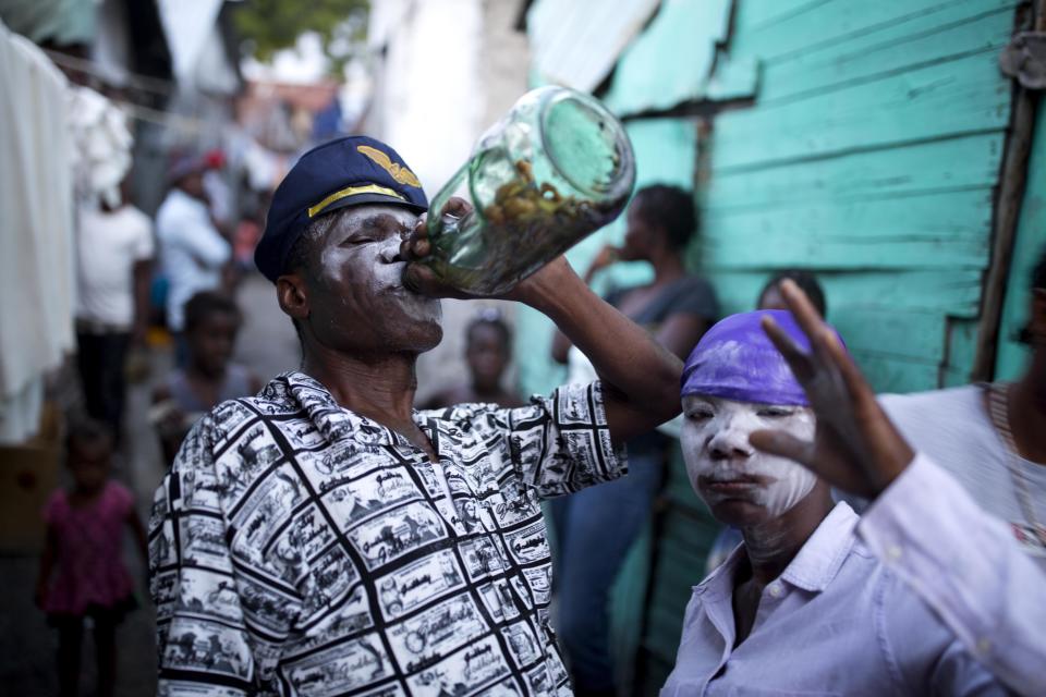 In this Oct. 31, 2018 photo, Raynold Alexandre, a voodoo priest, who is supposed to be possessed the Gede spirit, drinks with his daughter Darline Alexandre, also voodoo priestess, during Haiti's annual Voodoo festival Fete Gede, in Cite Soleil slum, in Port-au-Prince, Haiti. Alexandre and his wife Auguste are well known voodoo priests and three of their six children are also voodoo priests. ( AP Photo/Dieu Nalio Chery)
