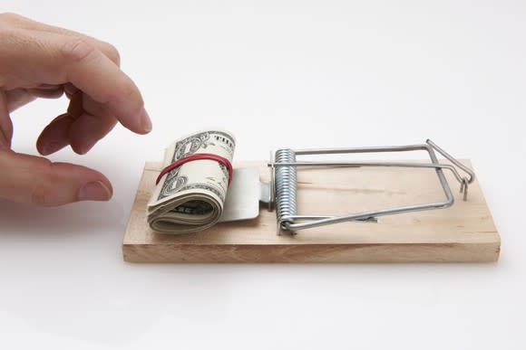 Hand reaching for money used as bait in a mousetrap.