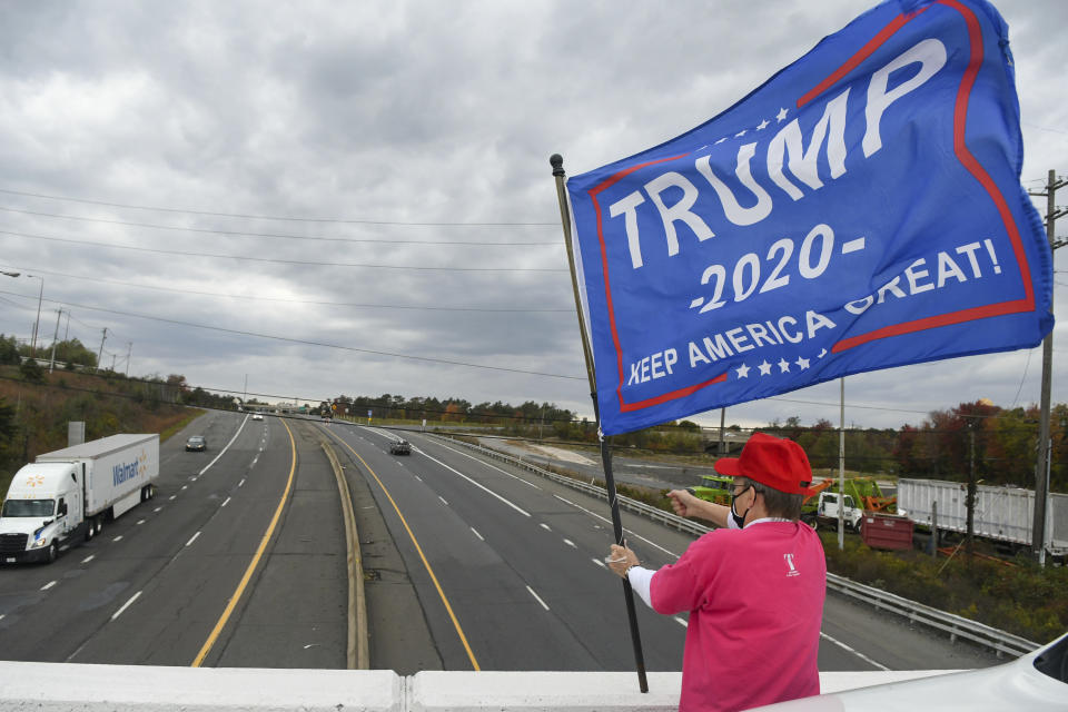 Carol Bylone, of Orwigsburg, Pa., signals for a trucker to honk while holding a Trump 2020 flag standing at the Schuylkill Mall Road bridge overlooking Route 61 during the Operation Flag Drop event in Frackville, Pa., on Wednesday afternoon, Oct. 7, 2020. (Jacqueline Dormer/Republican-Herald via AP)