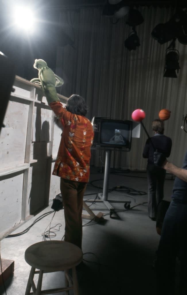 Jim Henson is seen puppeteering Kermit the Frog on set, while Frank Oz operates a different puppet in the background