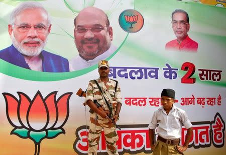 A policeman stands guard as a volunteer (bottom R) of the Hindu nationalist organisation Rashtriya Swayamsevak Sangh (RSS) looks on in front of a hoarding featuring Prime Minister Narendra Modi (L) and Amit Shah, president of India's ruling Bharatiya Janata Party (BJP), outside the venue of the party's national executive meeting in Allahabad, June 12, 2016. REUTERS/Jitendra Prakash