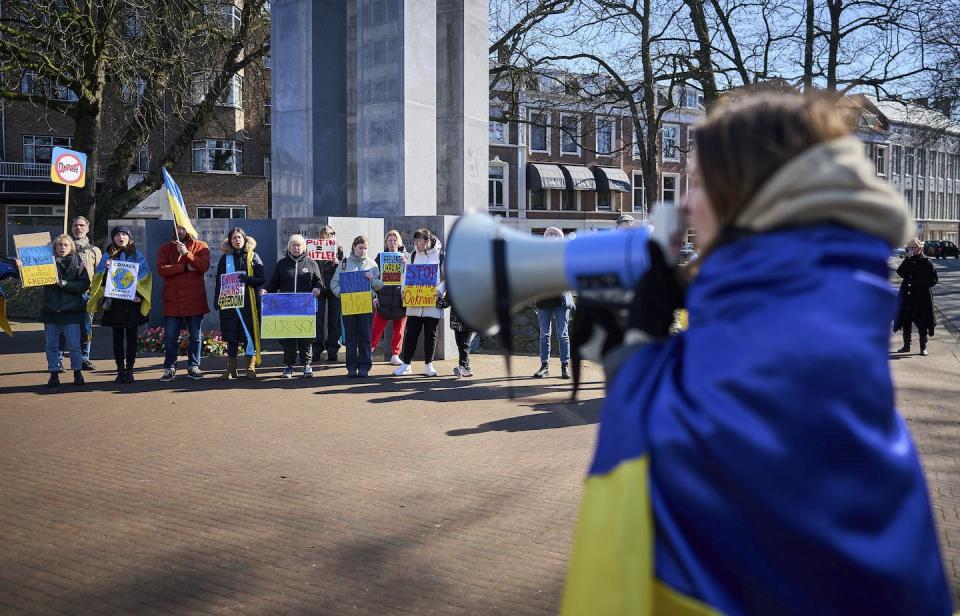 A woman wrapped in the Ukrainian flag shouts through a megaphone during a demonstration in front of the International Criminal Court in The Hague, Netherlands, in March 2022. (AP Photo/Phil Nijhuis)