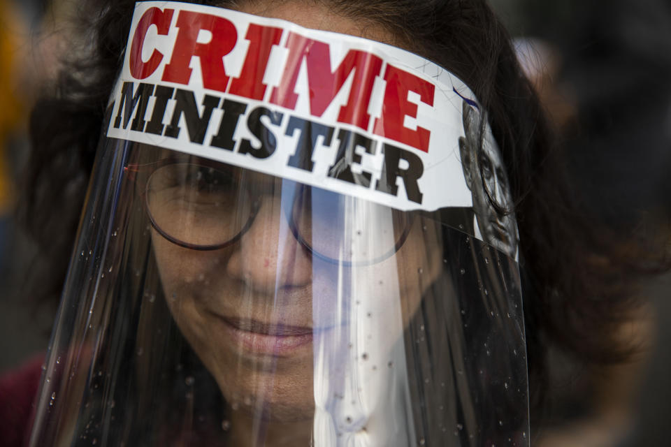 A protester against Israel's Prime Minister Benjamin Netanyahu wears a face mask during a protest outside his residence in Jerusalem, Sunday, May 24, 2020. Hundreds of protesters calling him the "crime minister" demonstrated outside his official residence, while hundreds of supporters, including leading members of his Likud party, rallied in support of him at the courthouse. Netanyahu faces charges of fraud, breach of trust, and accepting bribes in a series of corruption cases. (AP Photo/Ariel Schalit)