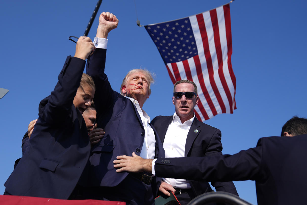 Donald Trump, surrounded by Secret Service agents, with a U.S. flag overhead, after his ear was grazed by a bullet at a campaign rally in Butler, Pa., on July 13.