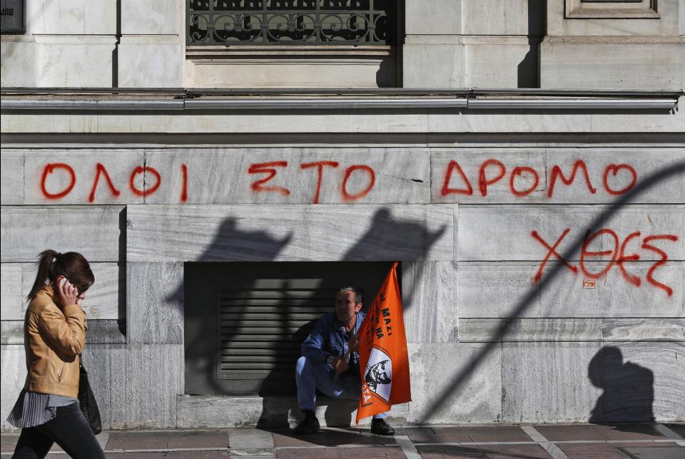 A municipal worker participating in a anti-austerity rally sits in front of the National Bank of Greece building, underneath graffiti reading in Greek "All to the streets yesterday", in central Athens, Friday, Nov. 9, 2012. Cash-strapped Greece will issue short term debt on Tuesday in the hope of raising enough money to repay a key bond days later. Greece is not expected to get its next batch of international rescue loans by Nov. 16, when it has to roll over 5 billion euros in three-month treasury bills. (AP Photo/Lefteris Pitarakis)