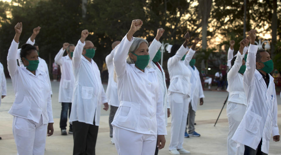 Una brigada de profesionales de la salud cubanos, que se ofrecieron como voluntarios para viajar a las Indias Occidentales, levantan el puño derecho mientras cantan el himno nacional de su país, en La Habana, Cuba, el sábado 28 de marzo de 2020. (Foto AP/Ismael Francisco)
