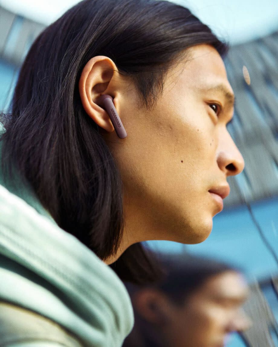 a person wearing the urbanears alby wireless earbuds in maroon