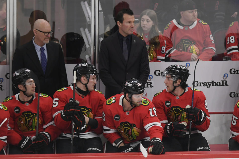 Chicago Blackhawks head coach Luke Richardson top center, looks on while Frank Nazar (91), Jason Dickinson (16) and Joey Anderson (15) talk on the bench during the first period of an NHL hockey game against the Carolina Hurricanes, Sunday, April 14, 2024, in Chicago. (AP Photo/Paul Beaty)