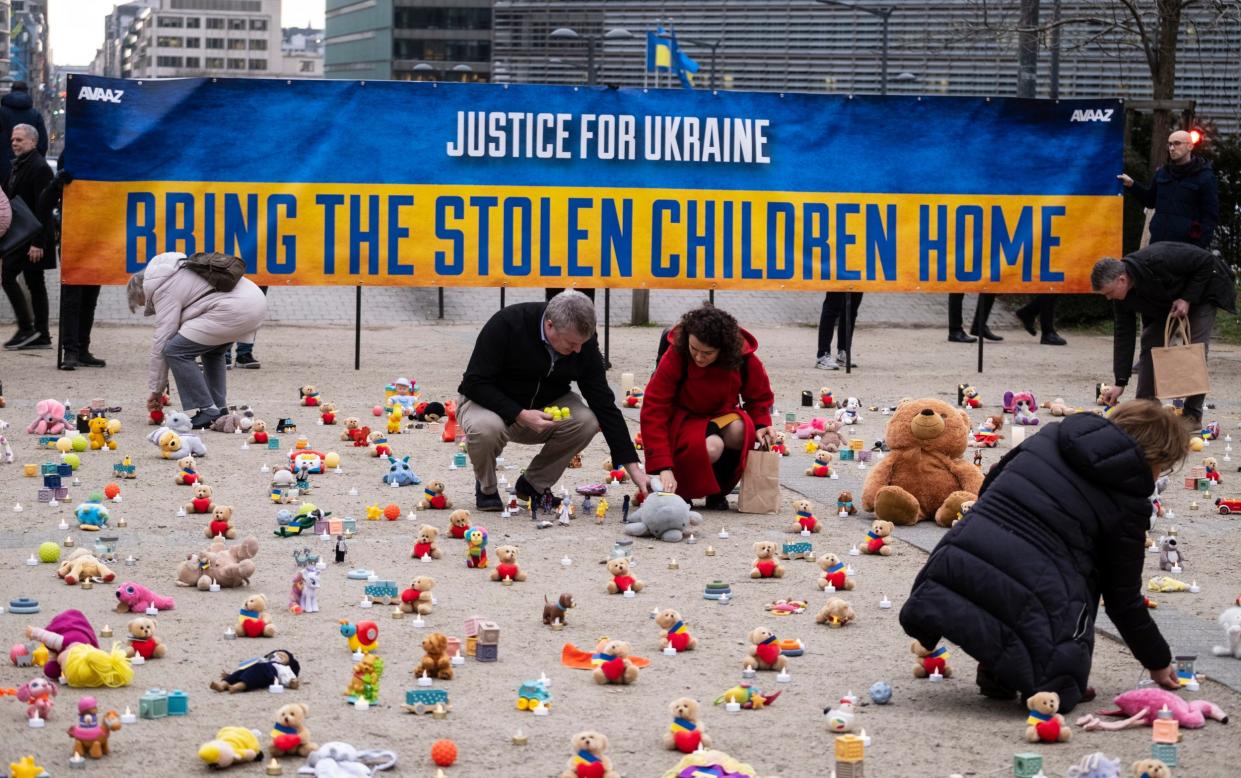 People lay out soft toys in grid form in a public square in Brussels, in front a banner reading 'Justice for Ukraine - Bring the Stolen Children Home'