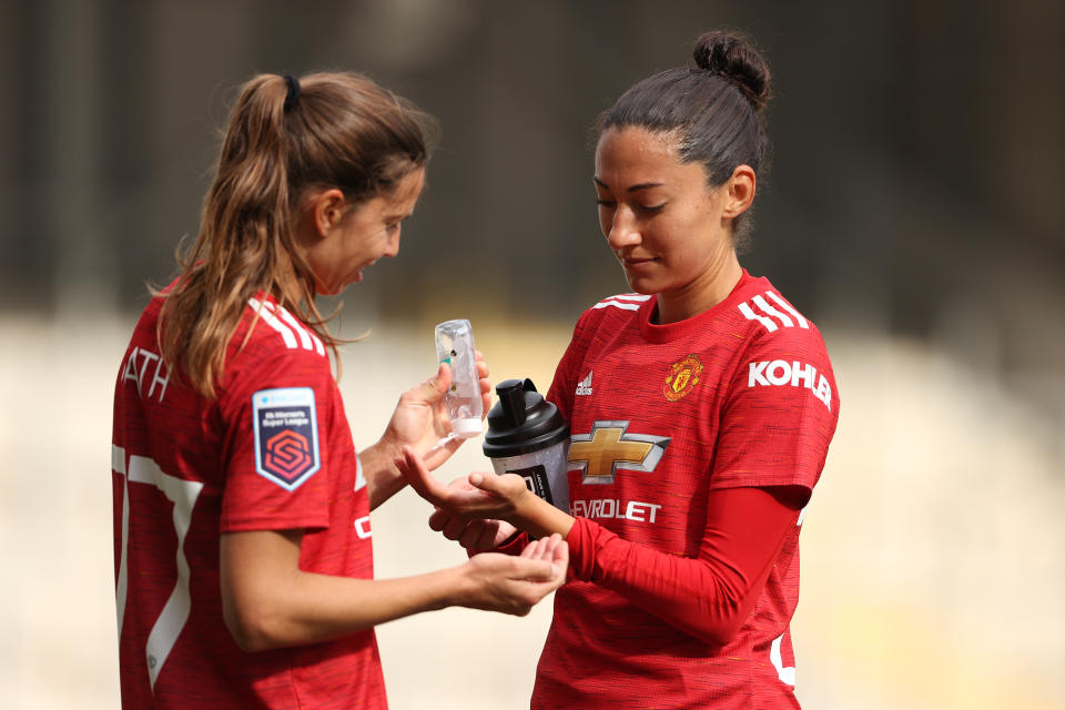 LEIGH, ENGLAND - OCTOBER 04: Tobin Heath of Manchester United Women applies hand sanitiser to the hands of Christen Press of Manchester United Women during the Barclays FA Women's Super League between Manchester United Women and Brighton & Hove Albion Women at Leigh Sports Village on October 4, 2020 in Leigh, England. (Photo by Matthew Ashton - AMA/Getty Images)