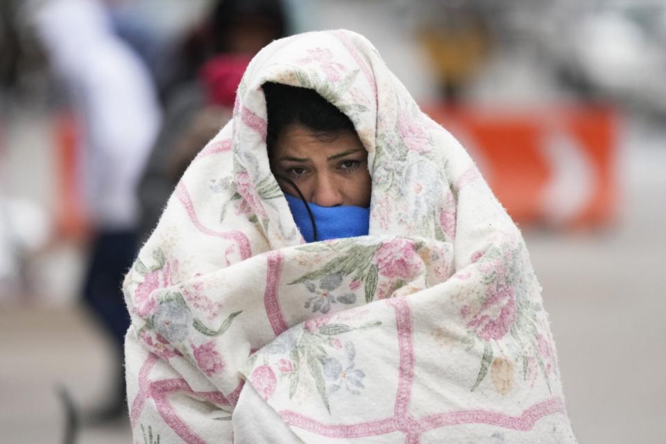 Photographed shoulders up, woman walks down a street, fully wrapped up in a white blanket with flower print.