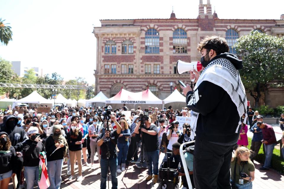 A person speaks with a bullhorn in front of a crowd on a campus.