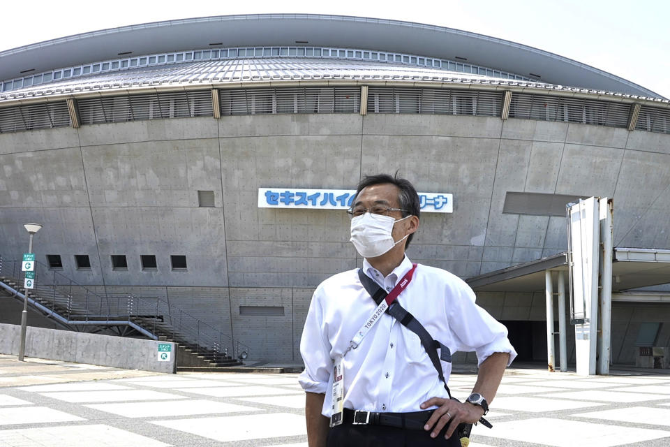 Olympic volunteer Atsushi Muramatsu poses for a photo in front of Sekisui Heim Super Arena, which was used as a morgue after the 2011 earthquake, also known as the Great East Japan Earthquake, in Rifu, Japan, Thursday, July 29, 2021. The arena is situated next to Miyagi Stadium, which is used for soccer matches during the 2020 Summer Olympics, where he is serving as a volunteer. Muramatsu has made business-card size flyers to express gratitude for support from overseas. He plans to hand them out to foreign media. (AP Photo/Chisato Tanaka)