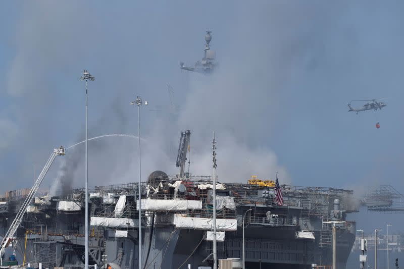 U.S. Navy helicopters and city firefighters continue fighting a fire on the amphibious assault ship USS Bonhomme Richard at Naval Base San Diego