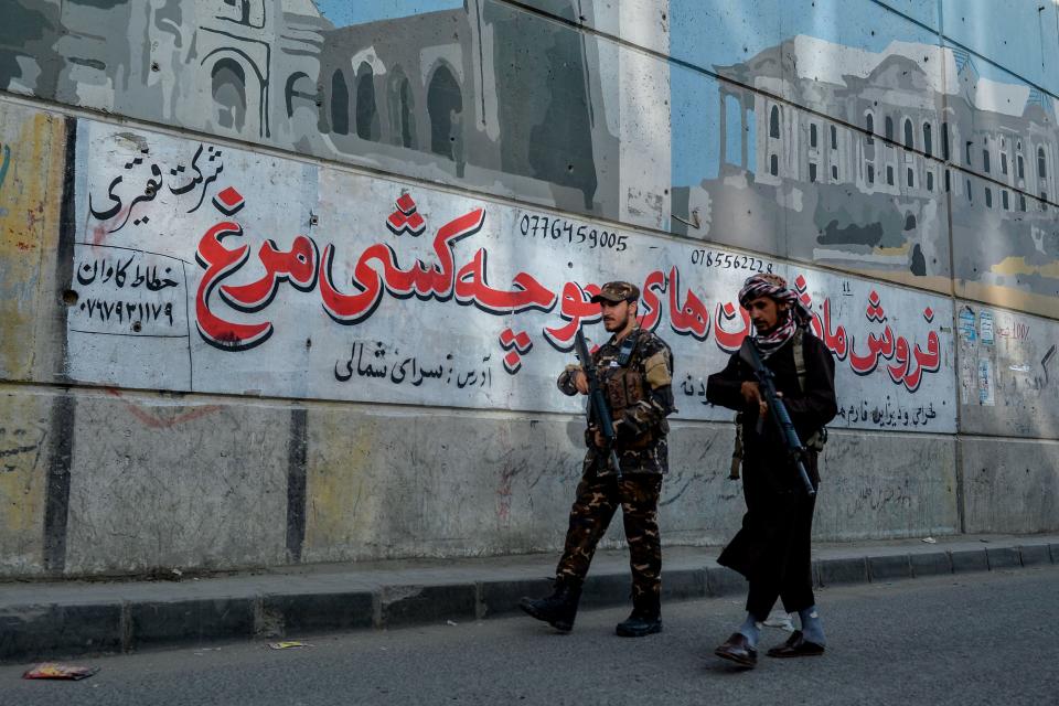 Taliban fighters patrol along a road on the backdrop of a mural pained on the wall of a flyover in Kabul on September 26, 2021